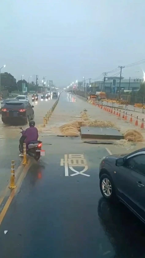 Floodwater surging around a displaced drain cover on a Kaohsiung road